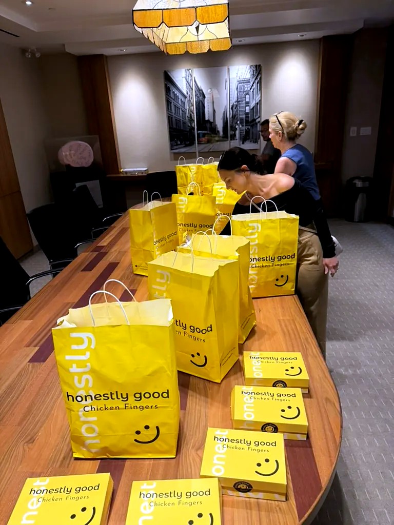 Honestly Good catering bags and boxes laid out along a boardroom table, being set up for an office lunch