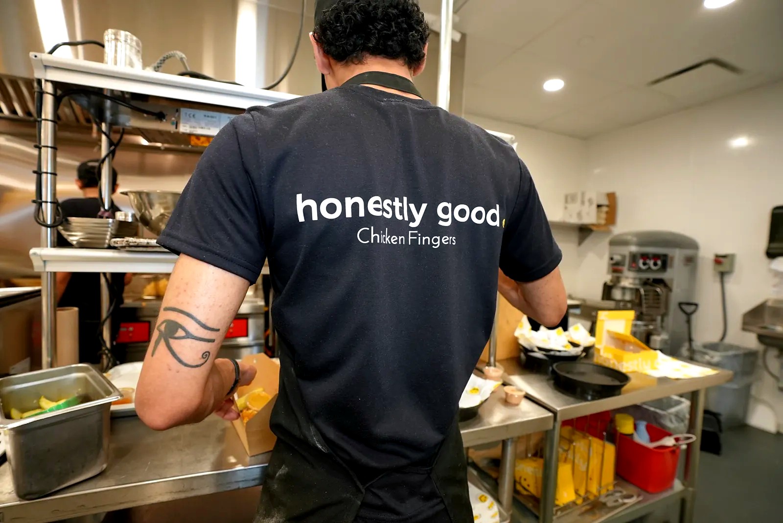 A cook in an Honestly Good apron boxing an order in the kitchen